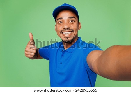 Close up delivery guy employee man wear blue cap t-shirt uniform workwear work as dealer courier do selfie shot on mobile cell phone show thumb up isolated on plain green background. Service concept