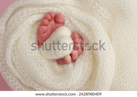 The tiny foot of a newborn baby. Soft feet of a new born in a white wool blanket. Close up of toes, heels and feet of a newborn. Knitted white heart in the legs of a baby. Macro photography 