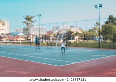 Blurred out of focus photo with a young child girl playing tennis and practicing on a tennis court. Sports photography. Great to be used as background concept photo.