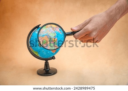 Picture of a globe with a magnifying glass magnifying countries, clear background with a hand placing the magnifying glass.