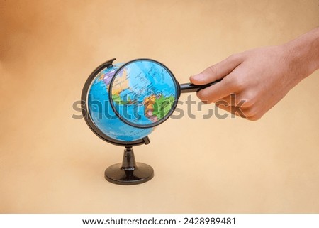 Shot of a globe with a magnifying glass magnifying countries, clear background with a hand placing the magnifying glass.