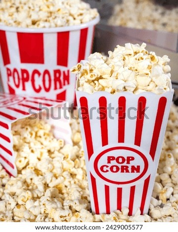 Popcorn inside of white containers with red stripes. Popcorn covers most of the picture with a slightly blurred background and props aligned in the golden ratio. Props include a popcorn maker.