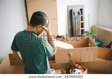 Back view of tired Man standing while looking at the cardboard boxes at home, preparation for moving out. Royalty-Free Stock Photo #2429006301