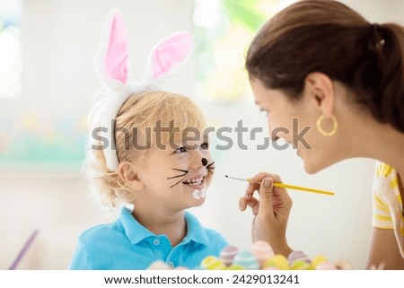 Mother and kids color Easter eggs. Face painting for little child. Little boy with bunny ears and mom dye eggs. Easter egg hunt. Family celebration and home decoration for spring holiday. Royalty-Free Stock Photo #2429013241