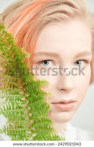 A cute blonde teenage girl with a short haircut in a summer sundress poses with green plant leave. Delicate spring-summer look. Beauty, natural cosmetics.
