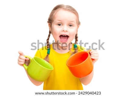 A cute girl in a yellow football shirt holds two large multi-colored mugs in her hands. White background