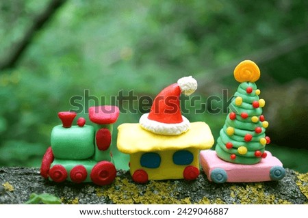 A toy train with a Christmas tree and a Santa Claus hat in the forest. Christmas toys made of plasticine.