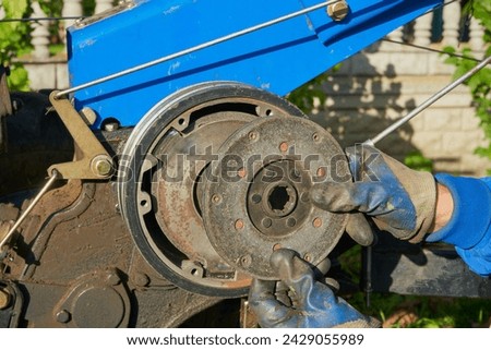 tractor clutch repair, holds a clutch disc in his hands against the background of a disassembled tractor, remove the clutch disc from the walk-behind tractor Royalty-Free Stock Photo #2429055989