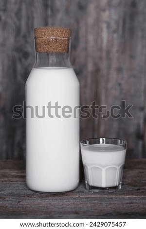 Rustic still life : a bottle of milk and a faceted glass in which milk is poured, next to black bread on a dark background