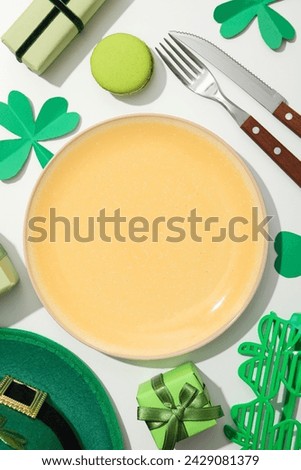 Cutlery, plate, gift boxes, clover leaves and green hat on white background, top view
