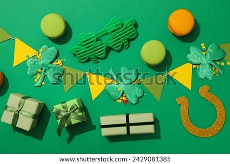 Clover leaves, paper flags, gift boxes and cookies on green background, top view