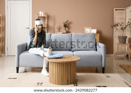 Injured young woman after accident talking by mobile phone at home Royalty-Free Stock Photo #2429082277