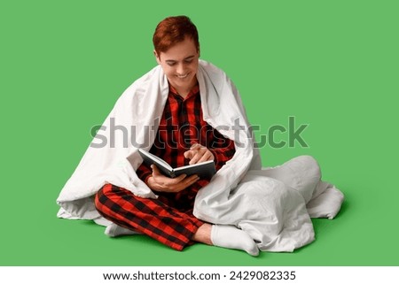 Handsome young happy man with blanket and book on green background