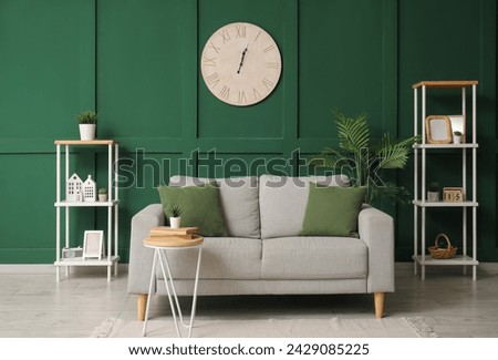Interior of stylish living room with comfortable sofa, houseplant, table, clock and shelves