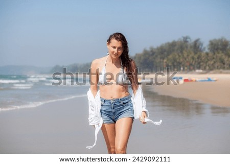 A beautiful girl with a wet hair and an Asian face type, a good slender figure posing on a sandy beach against the background of the ocean. Have fun 