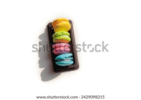 Picture of colorful macarons in a brown tray,4 pieces,yellow,green,pink, and blue,placed on a white table at different angles.It is a small, round dessert with a beautiful color and looks delicious.