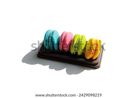 Picture of colorful macarons in a brown tray,4 pieces,yellow,green,pink, and blue,placed on a white table at different angles.It is a small, round dessert with a beautiful color and looks delicious.