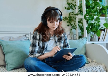 Young female teenager with digital tablet, stylus drawing illustrating sitting on couch at home