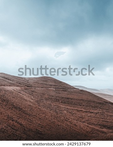 Layers of red and brown earth rise starkly against a dramatic sky, with a winding road cutting through the barren beauty of the Atlas Mountains. The raw, rugged terrain speaks of the earth's deep hist Royalty-Free Stock Photo #2429137679