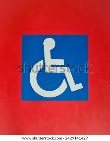 Blue and white painted wheelchair access sign for disabled people on red floor