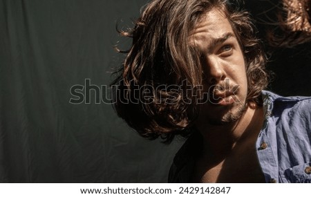A blonde male model with long hair looking at his reflection in the mirror