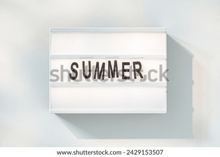A minimalistic lightbox displays bold black letters spelling out SUMMER, capturing the essence of the season with a dreamy sky backdrop.