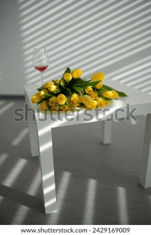 Beautiful yellow tulips on a white table with a glass.Sunlight. Background