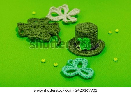 Handmade St. Patrick's Day concept. Traditional decorative symbols, pot with golden coins, crocheted four-leaf clover. Hard light, dark shadow, green background, close up