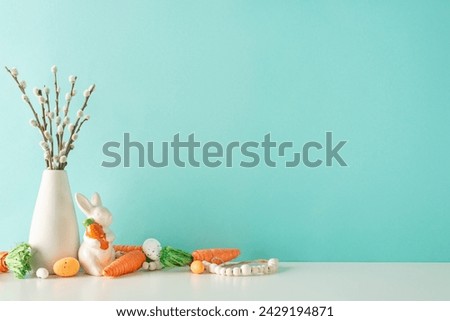 Easter display setup: Side view photo of a counter featuring a vase with pussy willow, a ceramic bunny figure, carrots for Easter bunny, assorted eggs, and beads on a pastel blue wall background
