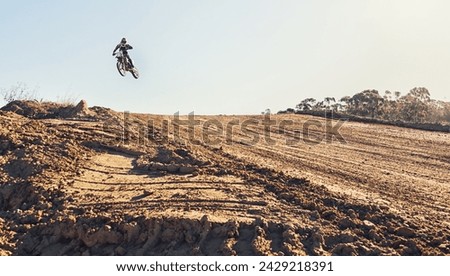 Person, jump and dirt track of professional motorcyclist in the air for trick, stunt or race on outdoor terrain. Expert rider on motorbike or scrambler for extreme sports with blue sky background