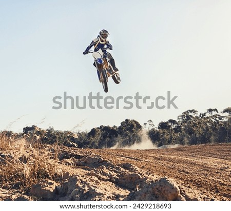 Person, jump and motorbike of professional motorcyclist in the air for trick, stunt or race on outdoor dirt track. Expert rider on bike or scrambler in dunes or extreme sport with blue sky background