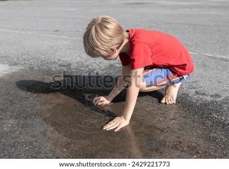 barefoot child plays with his hands in a transparent puddle on the asphalt. Sun after rain, change of weather in summer. Interesting, cheerful childhood, active lifestyle Royalty-Free Stock Photo #2429221773