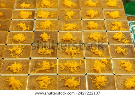 Uniformly arranged Thai dessert, Mo Kaeng, with small golden spheres made from egg yolks and sugar, set on square-cut, representing the traditional art of Thai dessert making