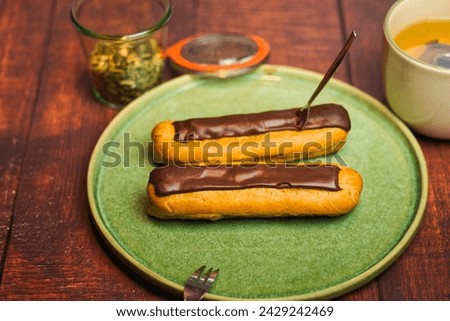Two eclairs on a wooden table with a cup of fresh tea. Eclairs are typical French pastries. 