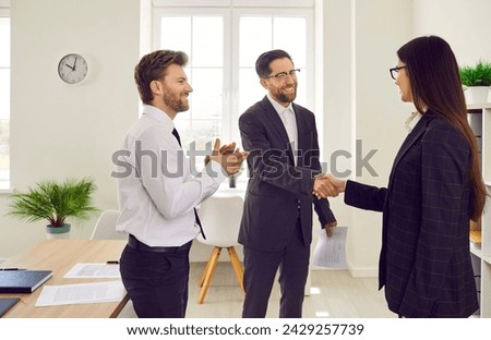 Group of a happy young three business people standing in the office making a good deal. Man shaking hands with woman reaching agreement or signing a contract or greeting new employee.