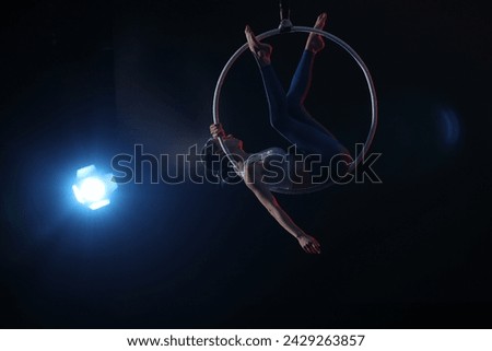Young woman performing acrobatic element on aerial ring against dark background. Space for text Royalty-Free Stock Photo #2429263857