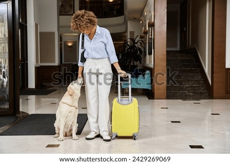 happy traveler with her Labrador in a pet-friendly hotel entrance, african american woman and dog Royalty-Free Stock Photo #2429269069