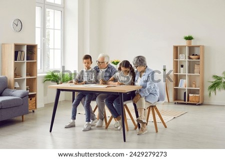 Family spending time together. Grandparents and grandchildren doing quiet indoor activites at home. Grandma, grandpa and children drawing pictures with colored pencils at table in living room interior