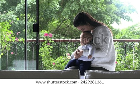 Mother kissing baby newborn baby infant next window overlooking nature