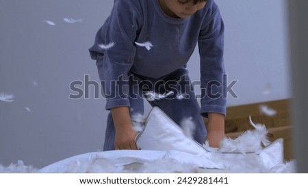 Feathers falling everywhere while little boy picks up unzipped pillow standing in bed wearing pajamas, child covered in plumage fly in air-SD 480p Royalty-Free Stock Photo #2429281441