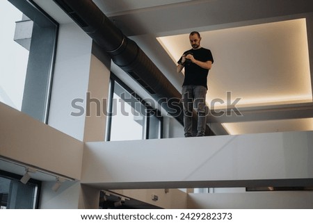 A professional photographer stands on an elevated platform indoors, intently capturing images with his camera.