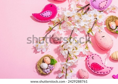 Gentle Easter composition with cherry flowers and handmade felt birds. Decorative eggs and nest, cute rabbits. Hard light, dark shadow, pink background, top view
