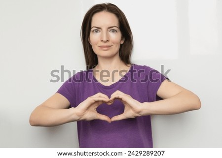 Inspire inclusion. Woman holding her hands in the shape of a heart and holding them in front of her, dressed purple t-shirt. International women's day concept.