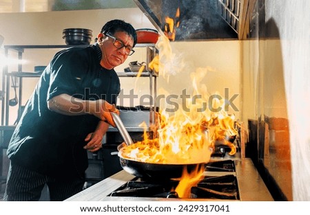 Chef in the restaurant kitchen making flambe in the frying pan. 
