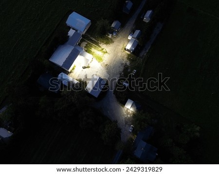 Overhead view at night of a farmstead with multiple buildings, their lights casting a soft glow on the surrounding yard and encroaching darkness of the fields. Royalty-Free Stock Photo #2429319829