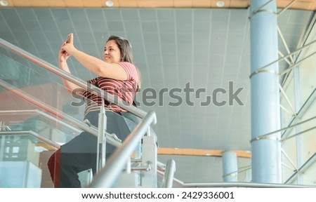 Selfie, young woman on airport stairs ready to travel, with a big smile. Smartphone for profile picture on social media app before boarding the airplane