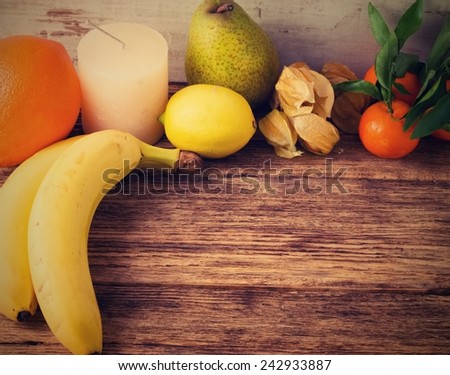 Vintage retro photo of table from old wooden board with different kinds of fruit as pear, orange, banana, gooseberry, mandarine and with one white candle.