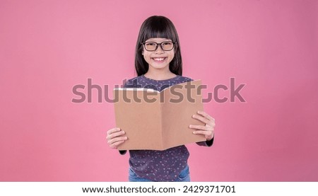 Portrait of little cute asian toddler nerd glasses girl reading book isolated on pink background, Education knowledgement. Nerd reader girl studying, home school and back to school concept