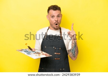 Young artist caucasian man holding a palette isolated on yellow background intending to realizes the solution while lifting a finger up
