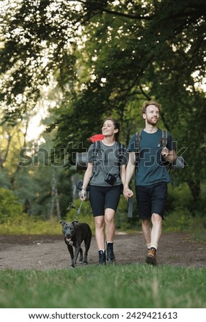 Photo of couple and a dog walking in forest at summer with backpacks